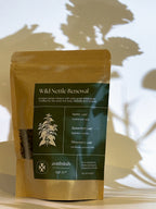 Tea package labeled 'Wild Nettle Renewal' on a wooden surface with a blurred natural background