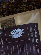 Tea packaging with 'Woodland Berry Tonic' label and herbal illustration.